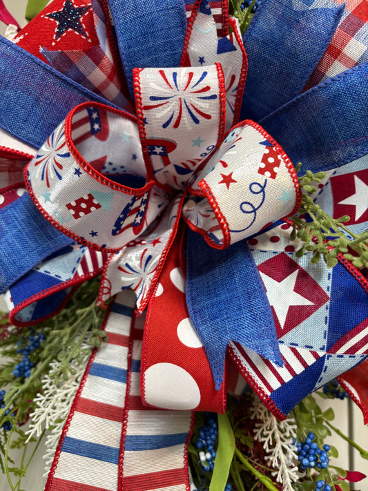 Patriotic greenery wreath featuring red, white, and blue ribbons with stars and stripes on a grapevine base.