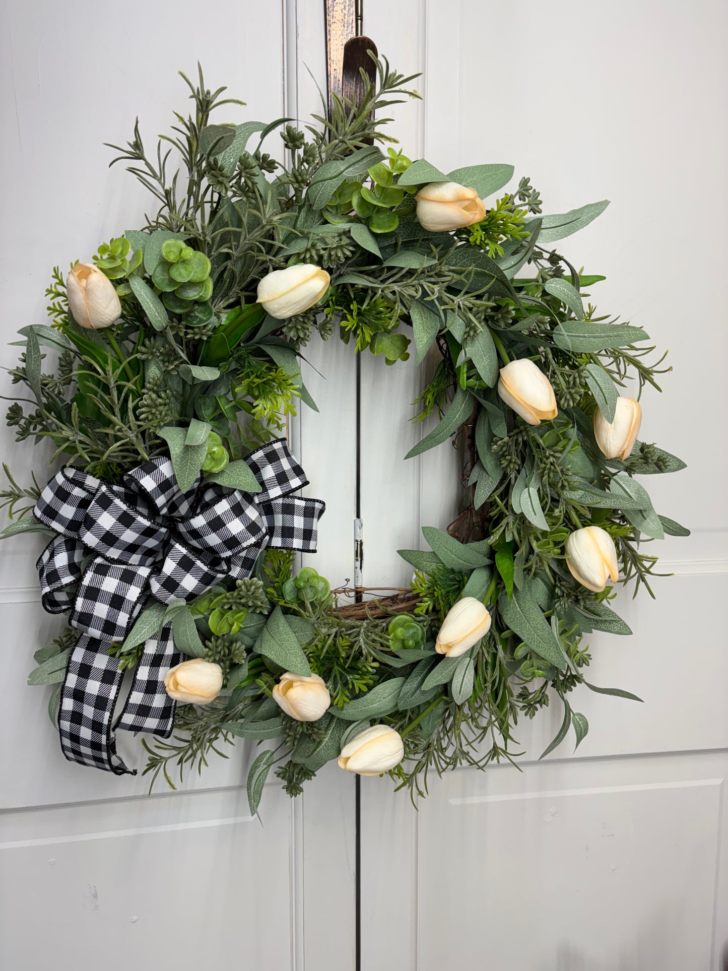 Spring tulip wreath featuring white tulips, eucalyptus, and a black and white checkered bow on a grapevine base.