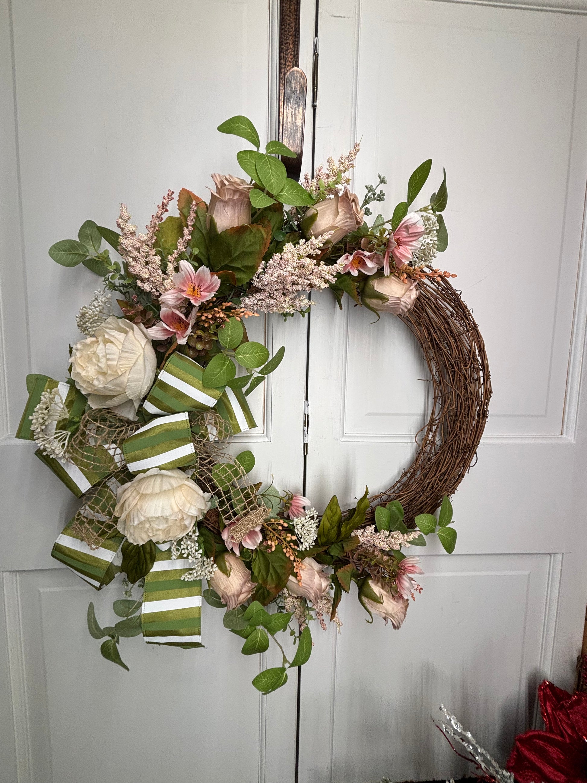 Spring peony and rose wreath with a bow, featuring pink and cream flowers on a grapevine base, hanging on a door.