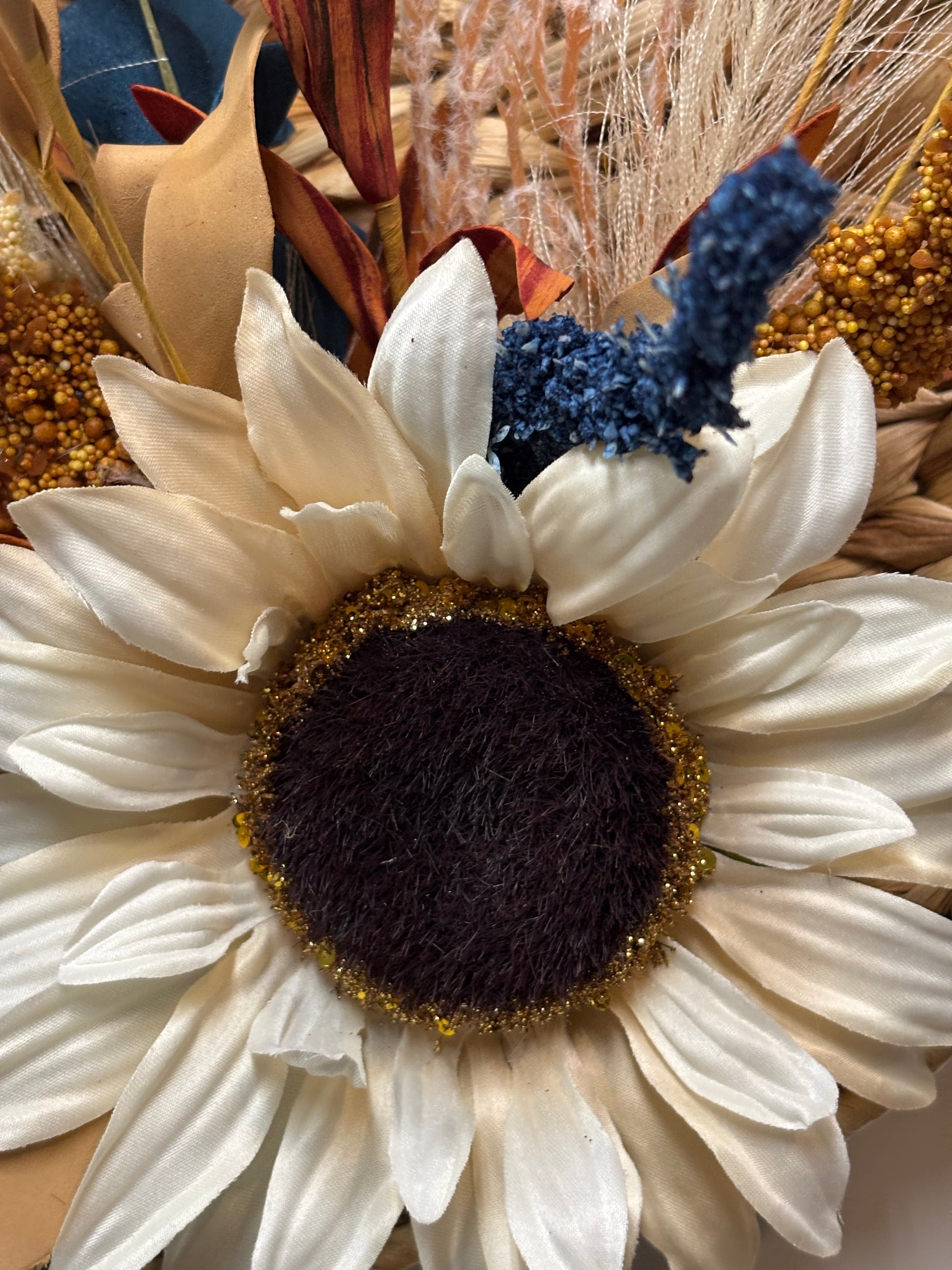 Woven pumpkin door hanger featuring a large sunflower, accented with dried flowers and autumn colors.