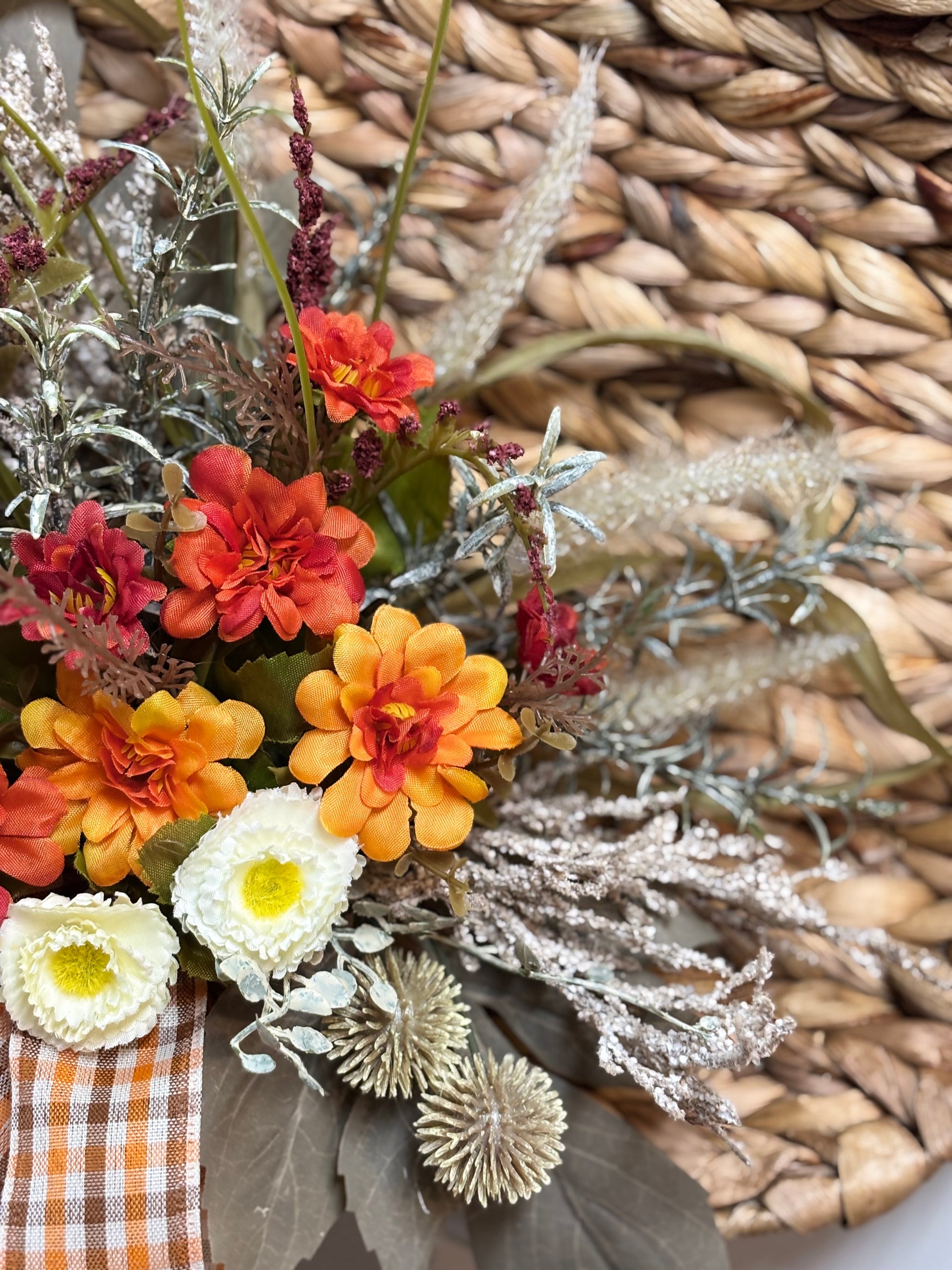 Woven pumpkin door hanger featuring orange and yellow flowers, silver accents, and a gingham bow on a textured background.